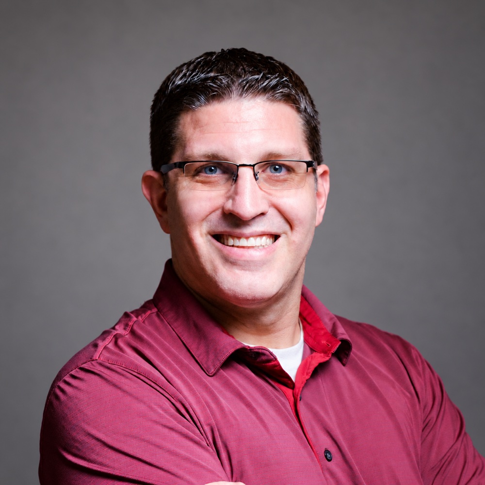 David Allen smiling, wearing glasses and a red shirt
